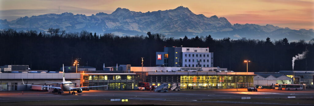 Der Flughafen Friedrichshafen am Bodensee in der Abenddämmerung vor Alpenpanorama mit Bergen.